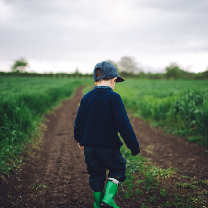 Photo of a little boy walking on a dirt road, spending time in nature