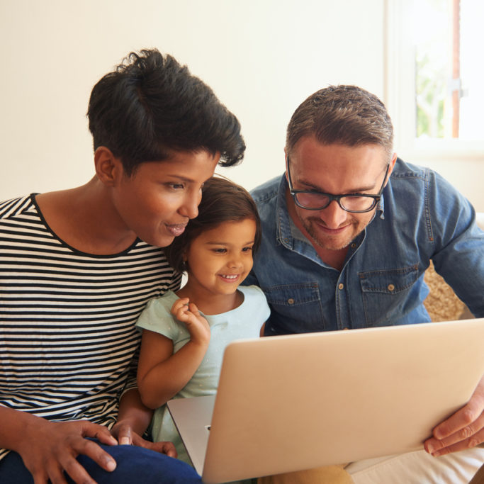 Cropped shot of a family of three using a laptop while sitting on their living room sofa